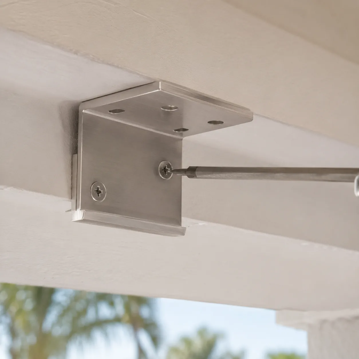 Brushed aluminum head-rail bracket being mounted to a lanai ceiling joist during exterior shade installation